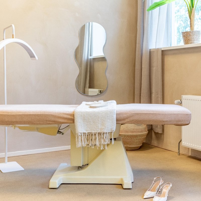 Behandelstoel met wenkbrauwlamp en golvende spiegel in de salon van Femmora Clinic